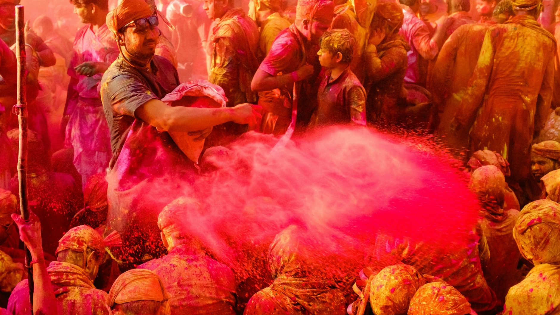 A burst of pink powder over the crowd in the temple courtyard at Barsana during Lathmar Holi