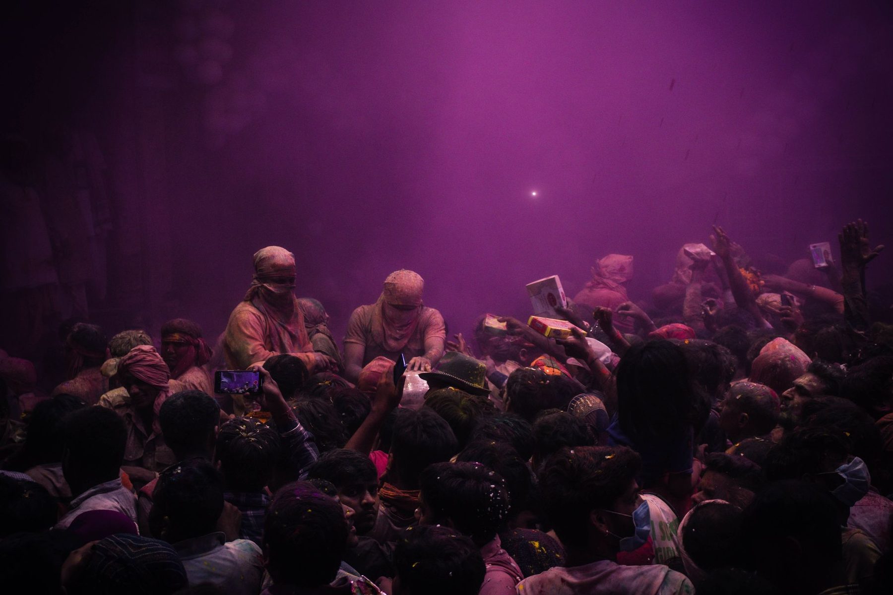 A crowd in Vrindavan after dark during Holi week, lit in red and pink through a haze of powder