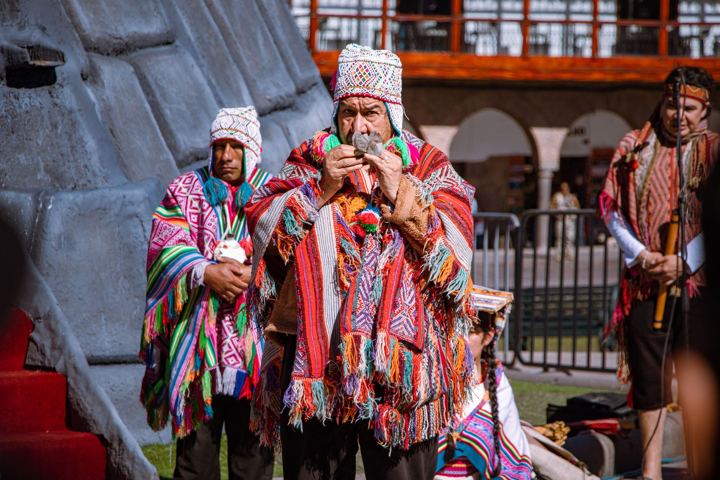 Men in woven ponchos and chullo hats making a coca-leaf offering in the Plaza de Armas of Cusco in June