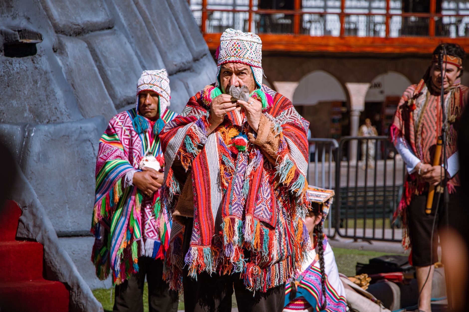 Men in woven ponchos and chullo hats making a coca-leaf offering in the Plaza de Armas of Cusco in June