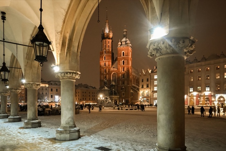 St Mary's Basilica at night across a snowy main square in Kraków, framed by the arcade of the Cloth Hall