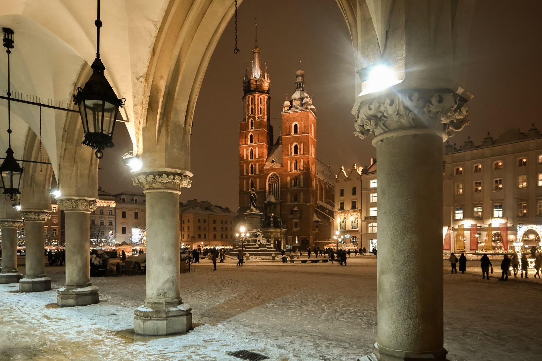 Wooden market stalls and a tall lit Christmas tree in front of the Cloth Hall on Kraków's main square at night