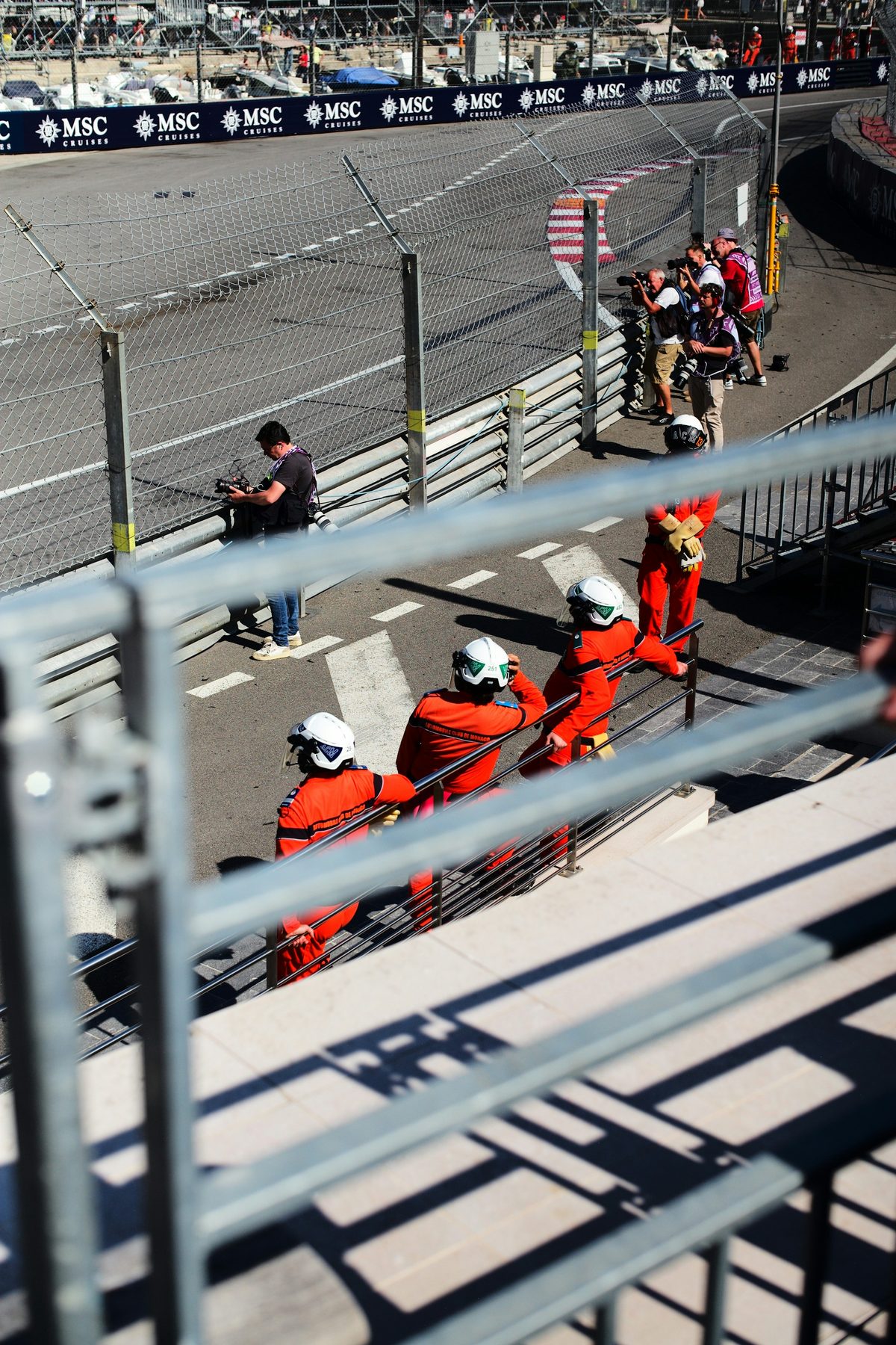 Marshals in orange sitting at their post beside the Monaco circuit, the harbour stands behind them