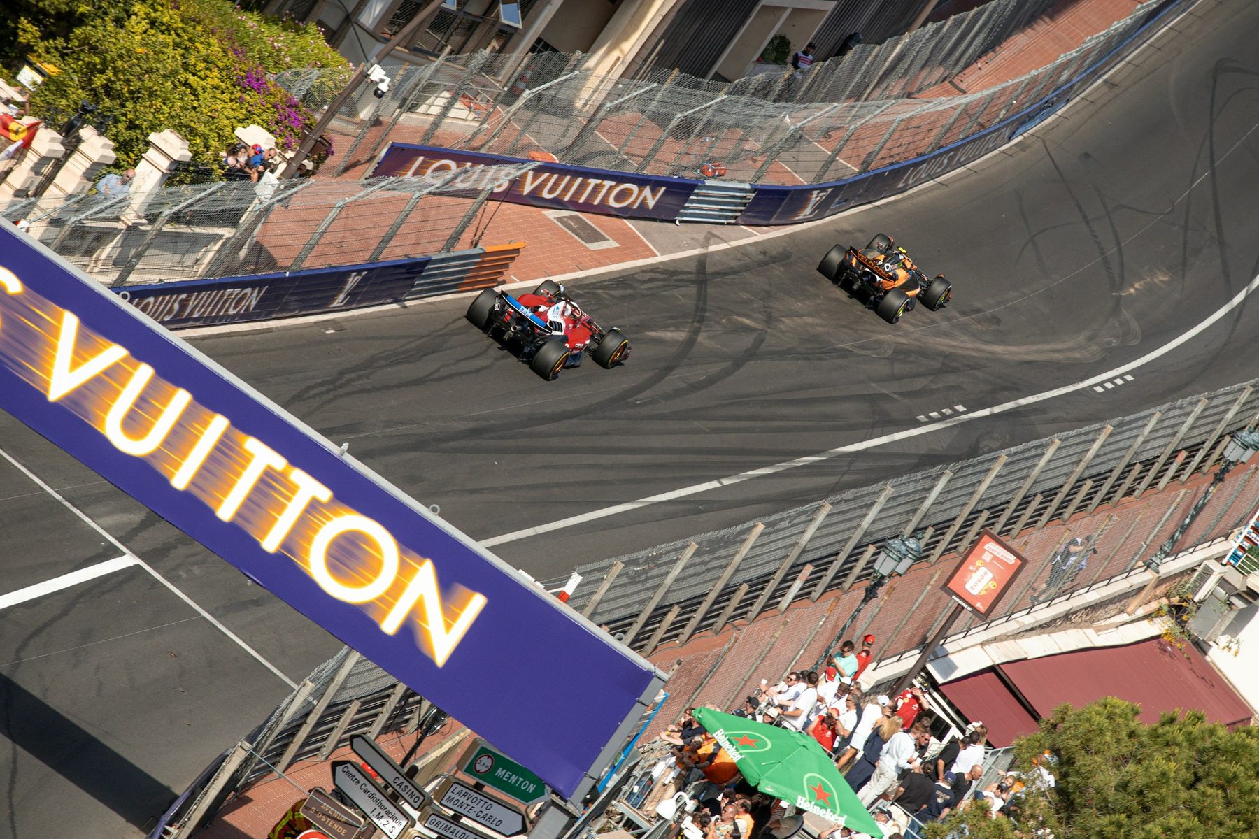 Two Formula 1 cars passing under the Louis Vuitton bridge on the Monaco circuit, tyre marks on the road