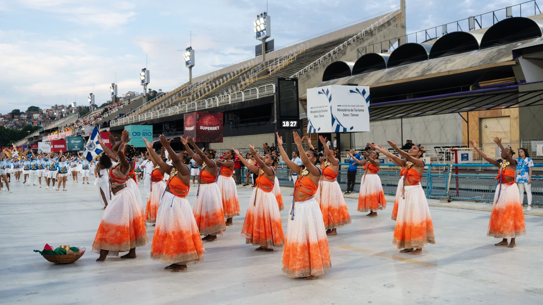 Dancers in orange and white skirts on the Sambadrome avenue in Rio de Janeiro, with the concrete stands behind