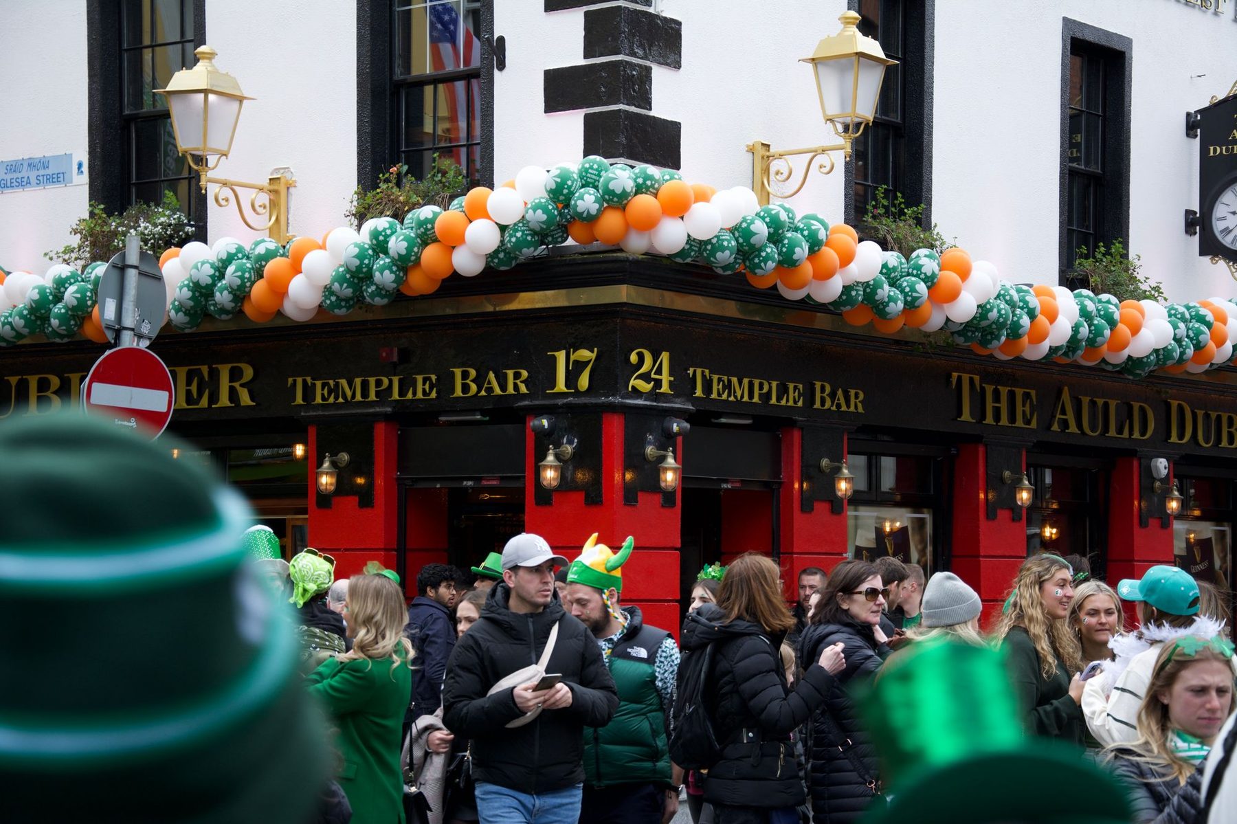 A crowd in green hats outside a Temple Bar pub hung with green, white and orange balloons on St Patrick's Day in Dublin