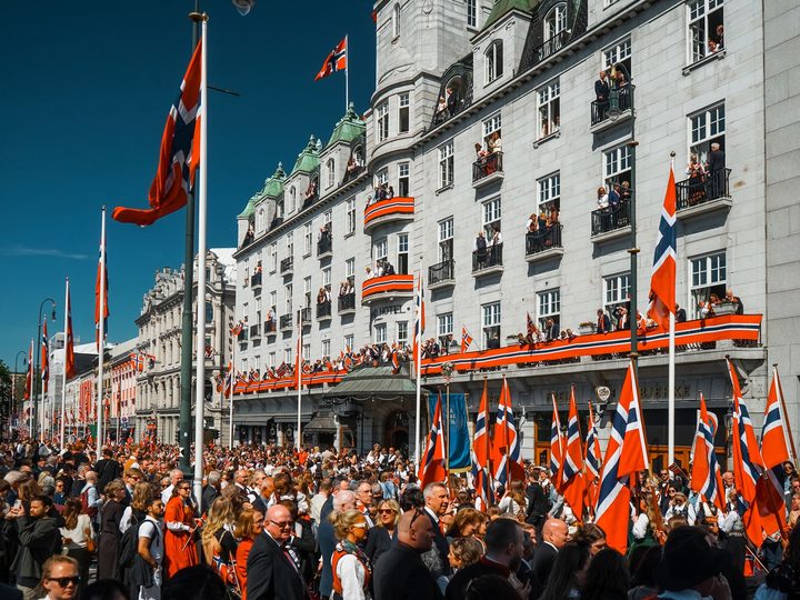 Crowds and Norwegian flags on Karl Johans gate in Oslo on Constitution Day, with spectators on the balconies of the Grand Hotel