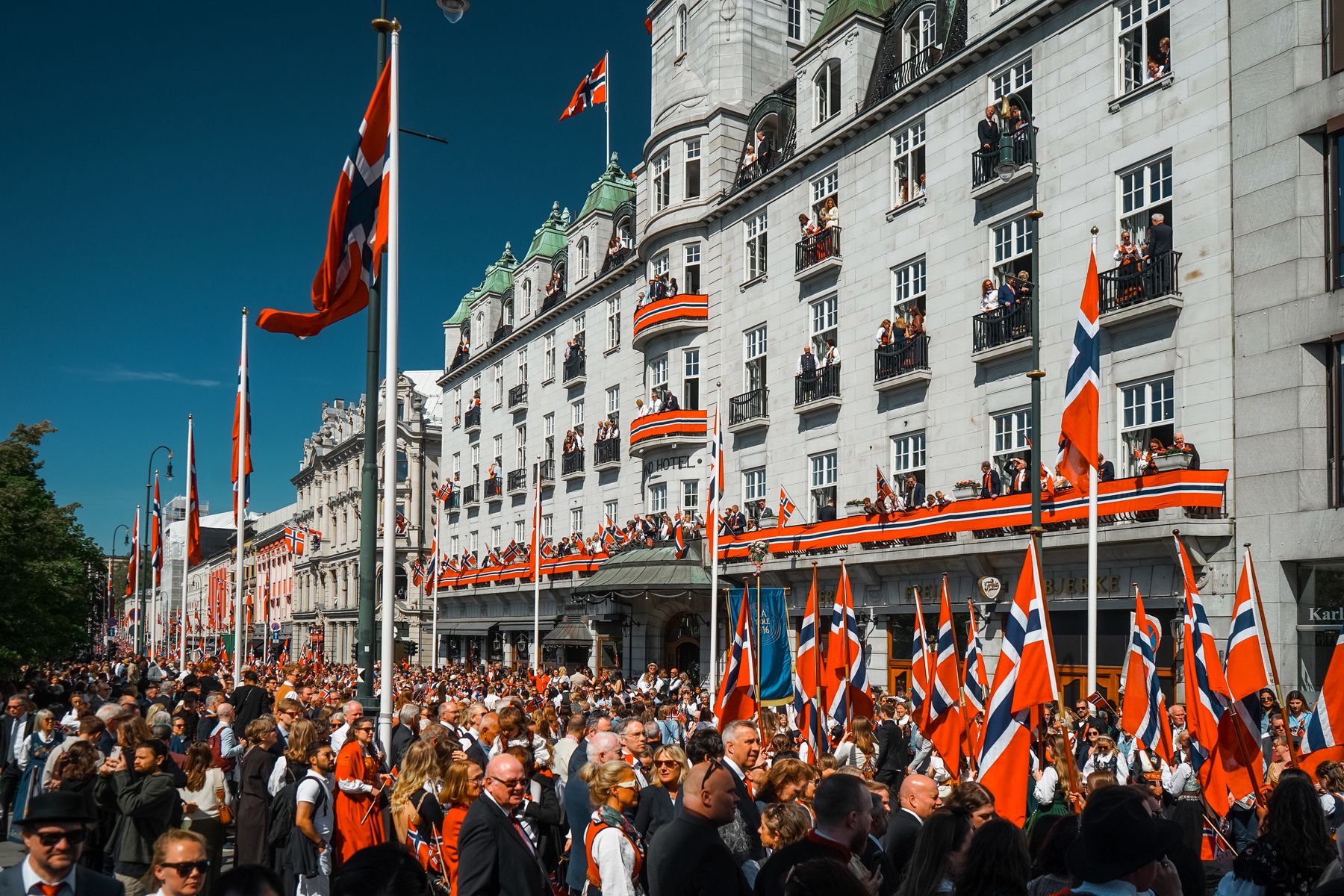 Crowds and Norwegian flags on Karl Johans gate in Oslo on Constitution Day, with spectators on the balconies of the Grand Hotel