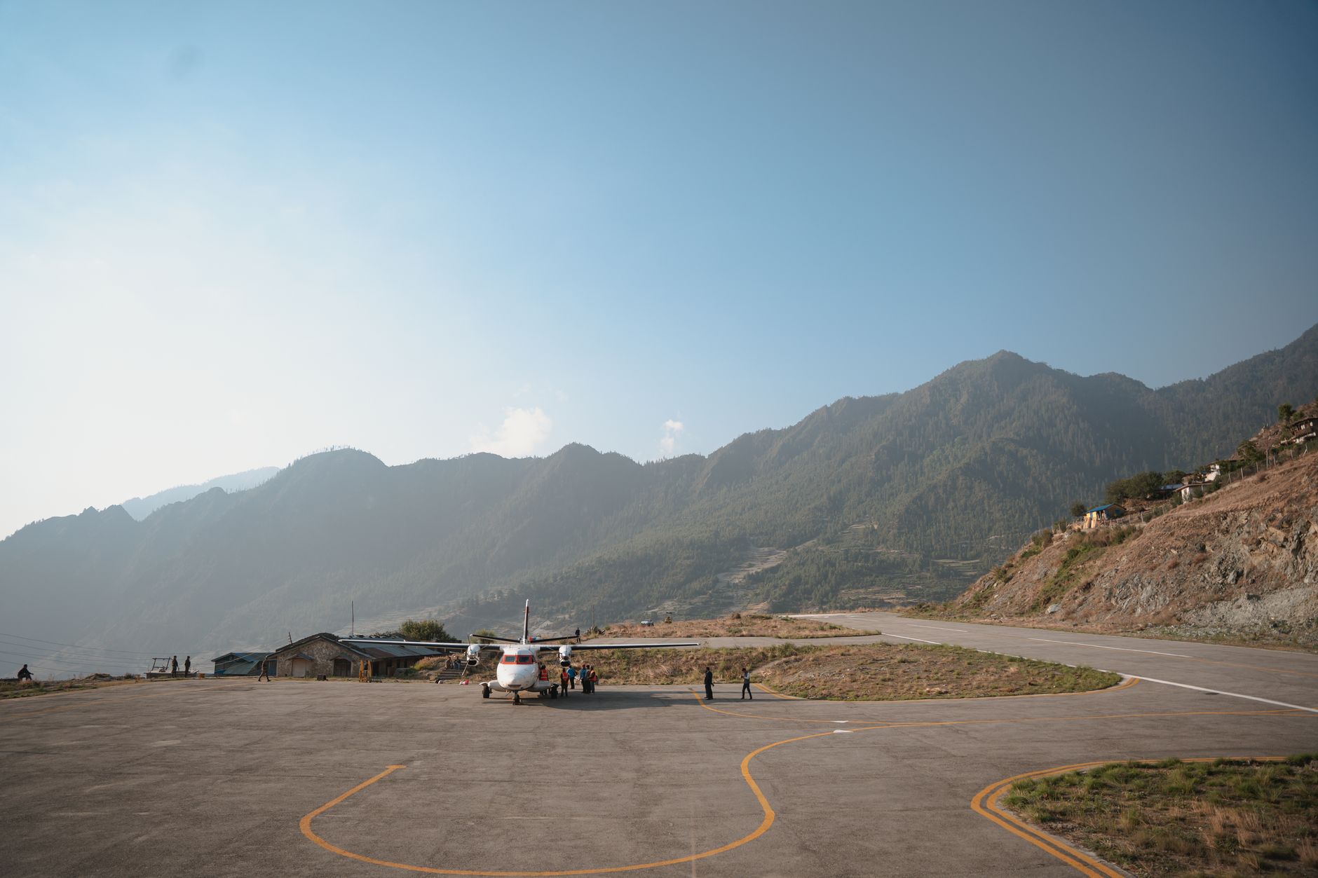 Small aircraft parked on the apron at Lukla airport with Nepali hills behind