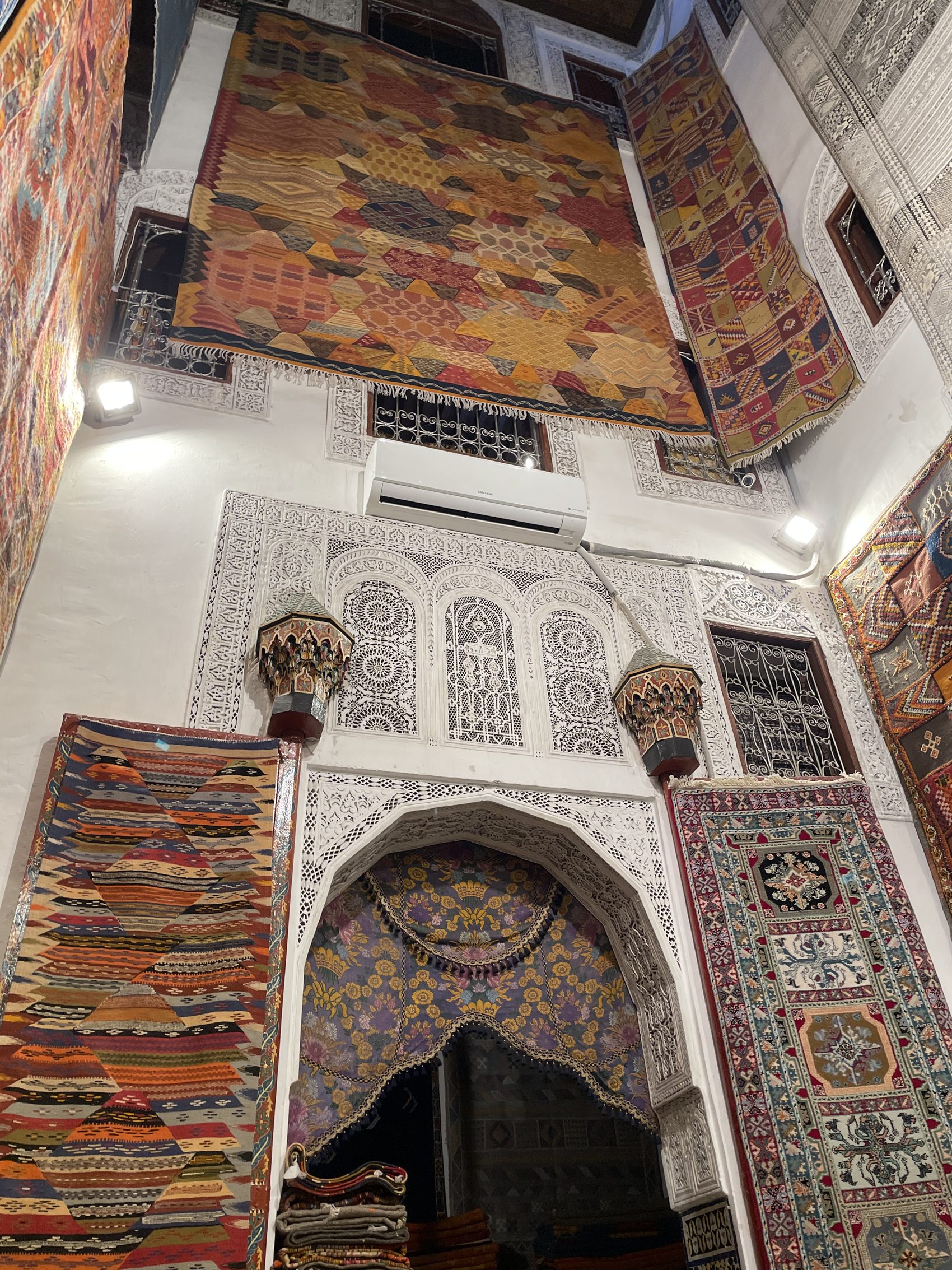 The interior of a carpet shop in Fez hung with kilims and rugs around a carved alcove