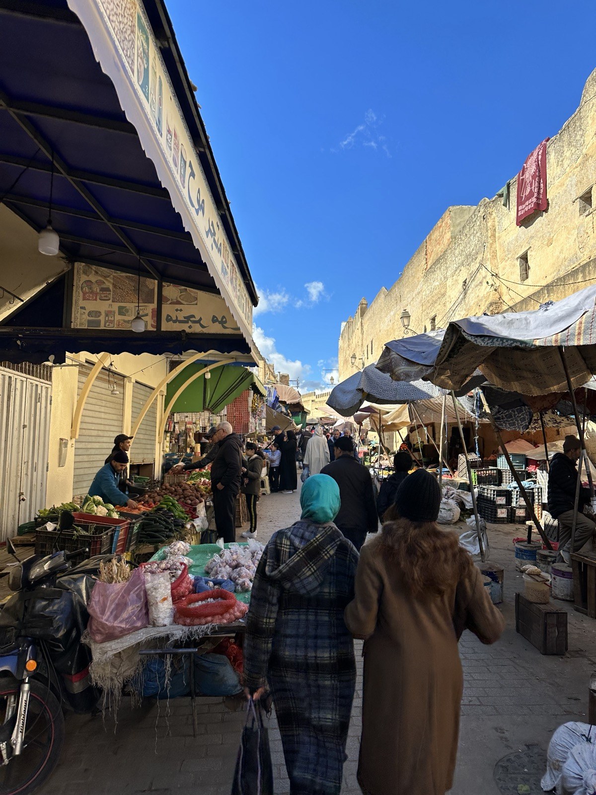A vegetable market in the Fez medina in winter, shoppers in heavy coats among stalls of produce