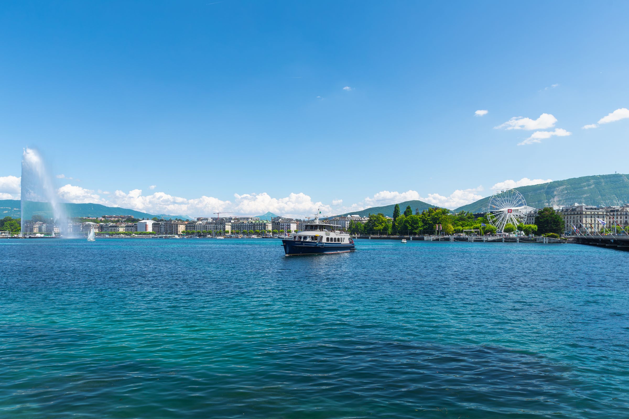 Geneva's harbour from the Pâquis shore, the Jet d'Eau on the left, a lake launch in the middle and the Salève behind the Jardin Anglais and its wheel