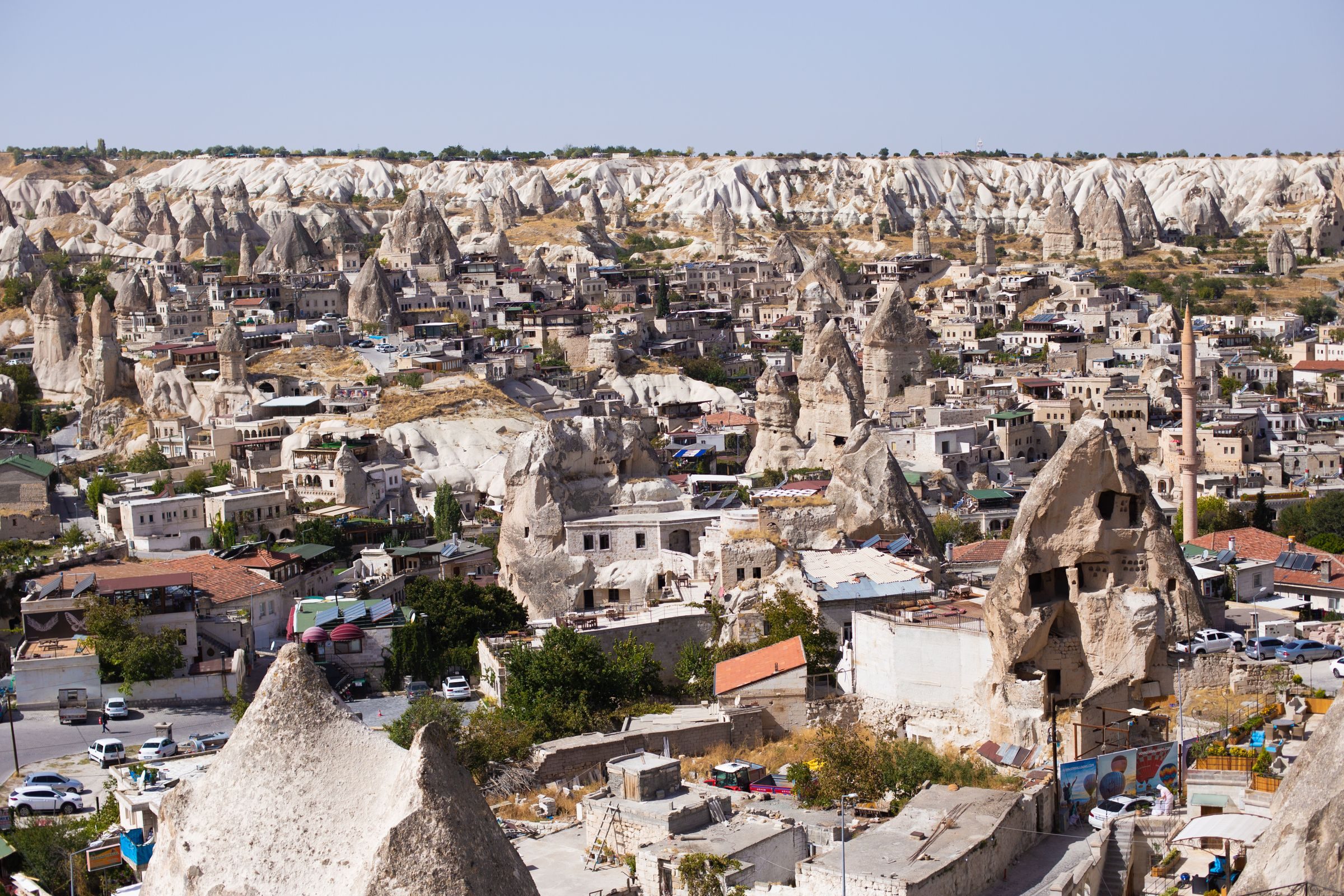 Göreme village among its fairy chimneys, cave houses cut into the cones, a minaret above the roofs and the pale valleys beyond