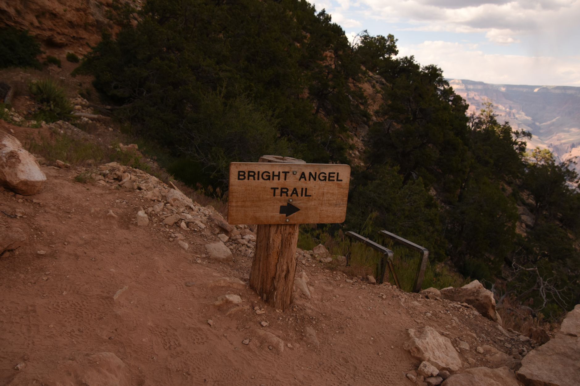 A wooden Bright Angel Trail sign beside the dusty switchbacks descending below the Grand Canyon's South Rim