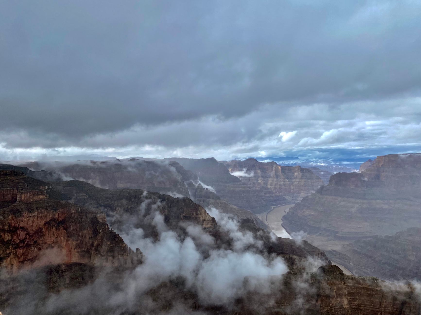 Cloud pouring into the Grand Canyon below the rim and filling the side canyons, with the river visible beyond