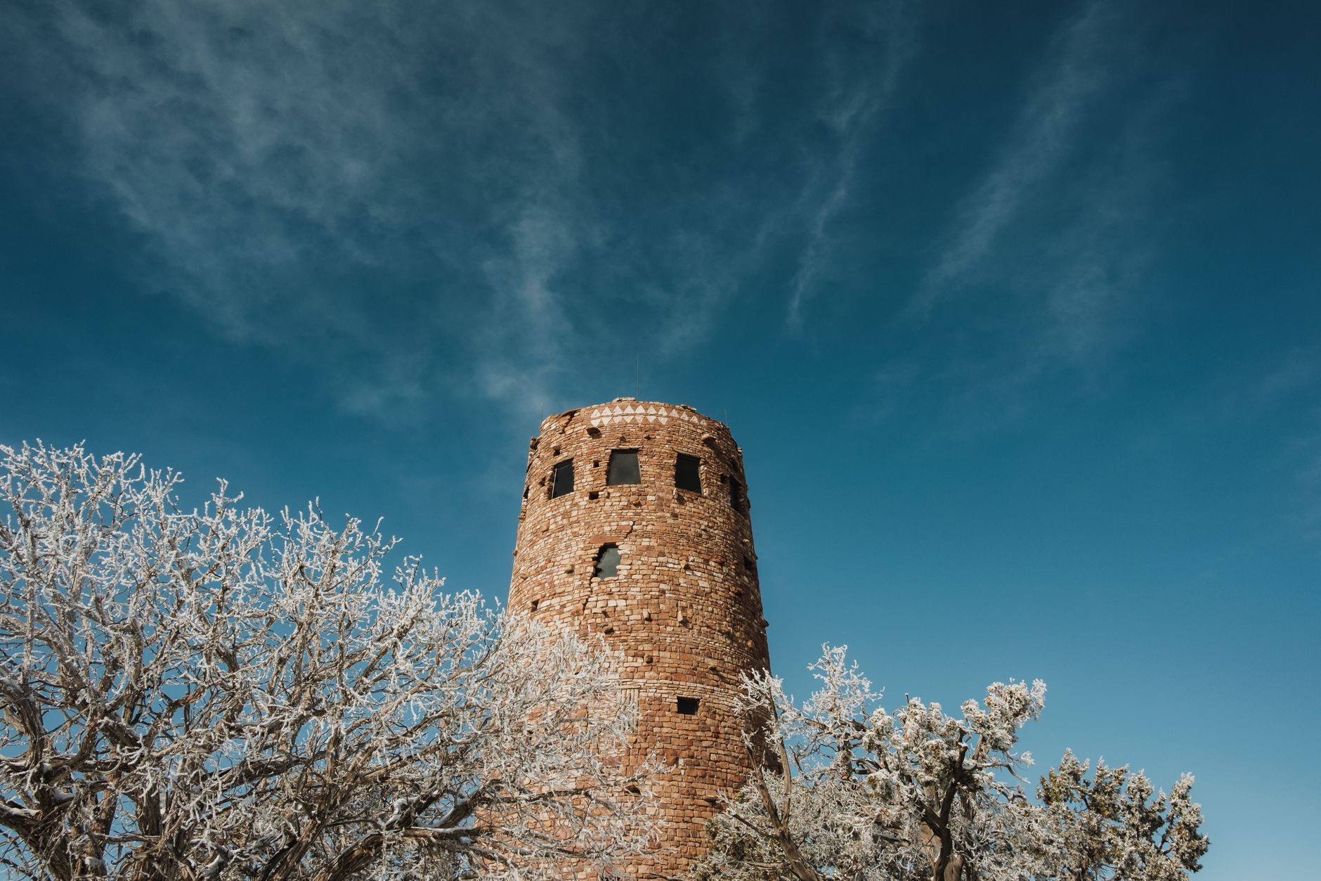 The stone Desert View Watchtower at the Grand Canyon rising above desert scrub against a deep blue sky
