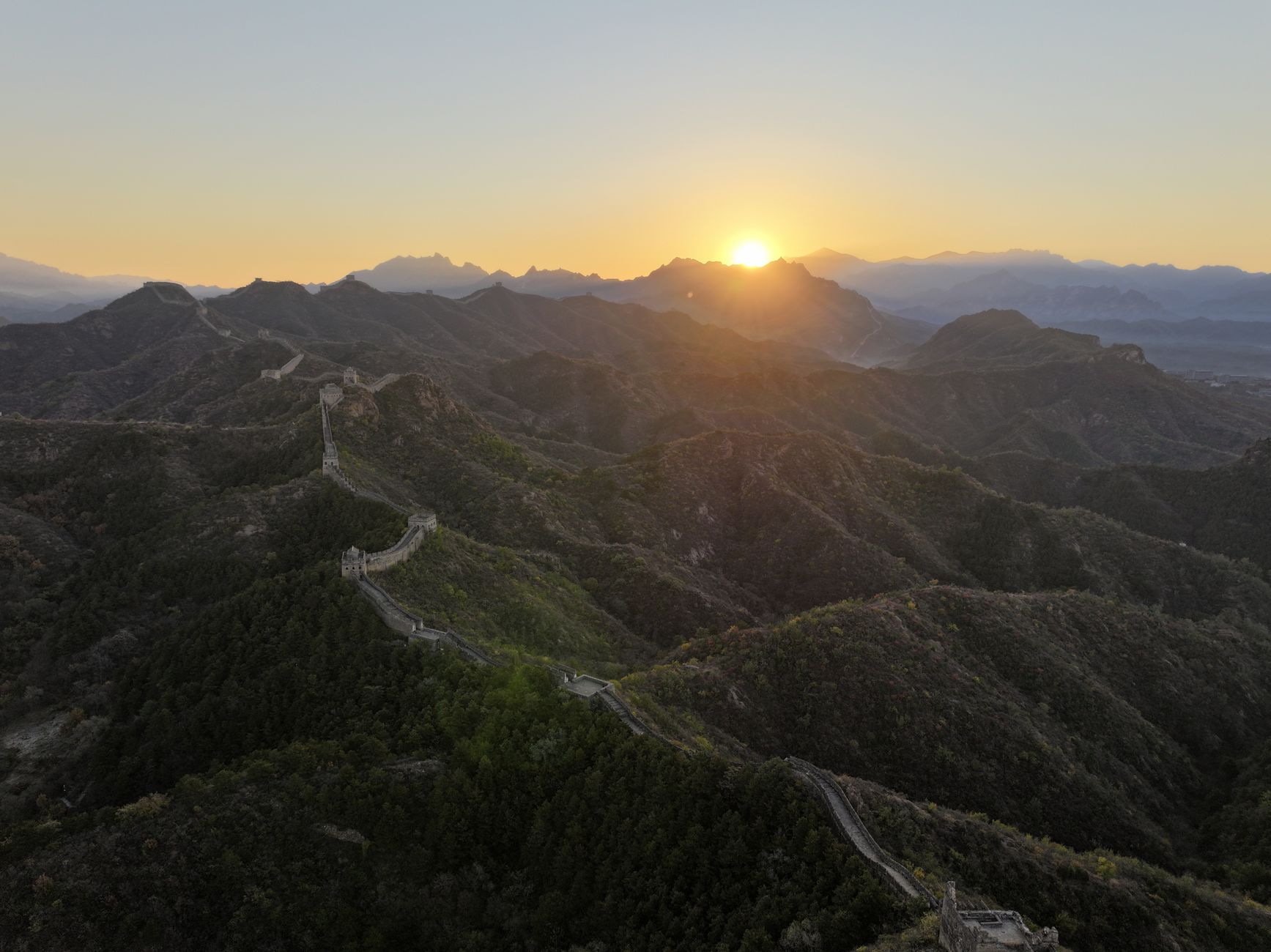 Sunrise over the Great Wall winding across forested mountains