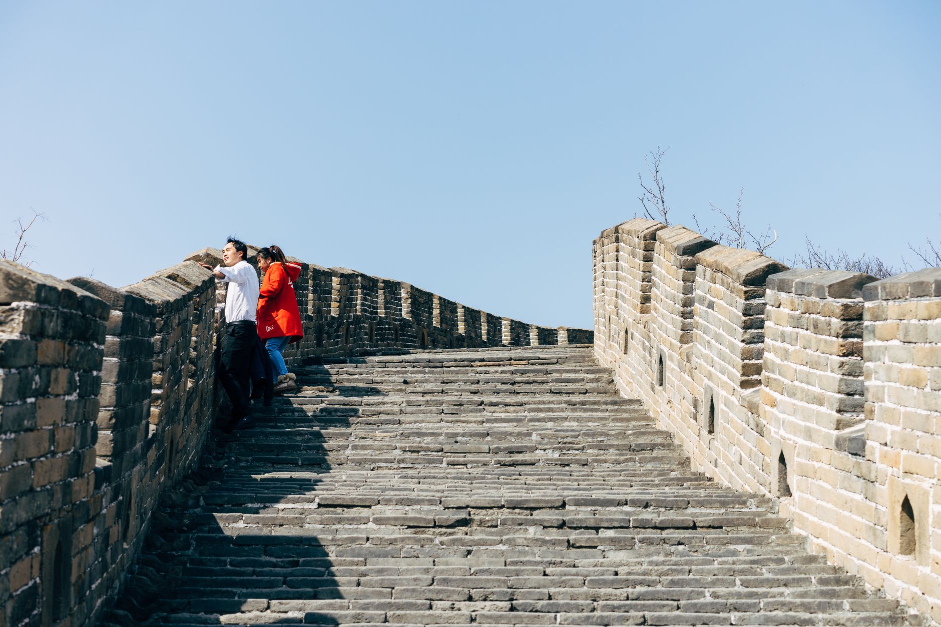 Visitors climbing a steep restored stair on the Great Wall under a blue sky