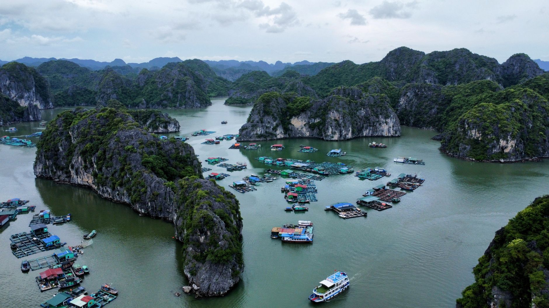 Aerial view of a floating fishing village of moored rafts and pens between limestone islands in Ha Long Bay