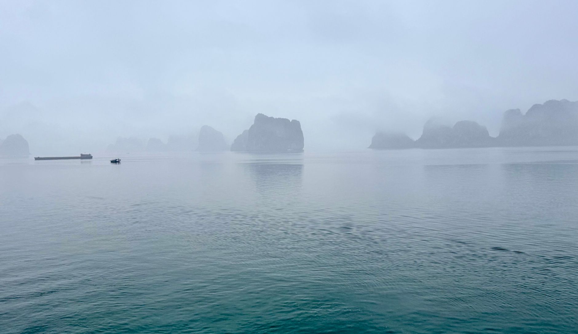 Limestone towers dissolving into grey mist over flat water at dawn in Ha Long Bay