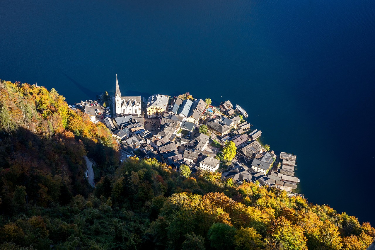 Hallstatt seen from above in autumn, houses stacked down a gold and green slope to the dark blue lake