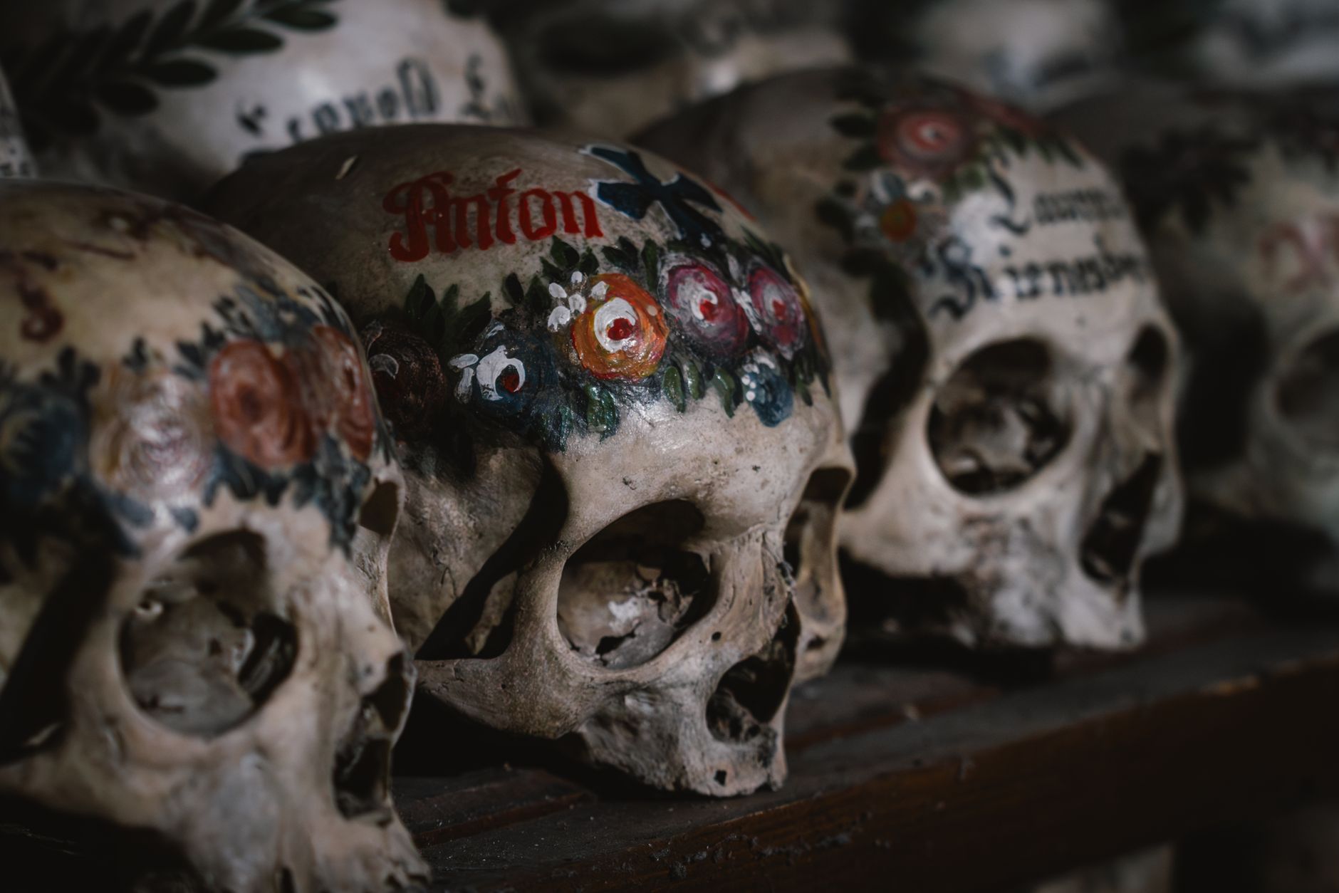 Painted human skulls with names and floral wreaths lined up in the Hallstatt ossuary