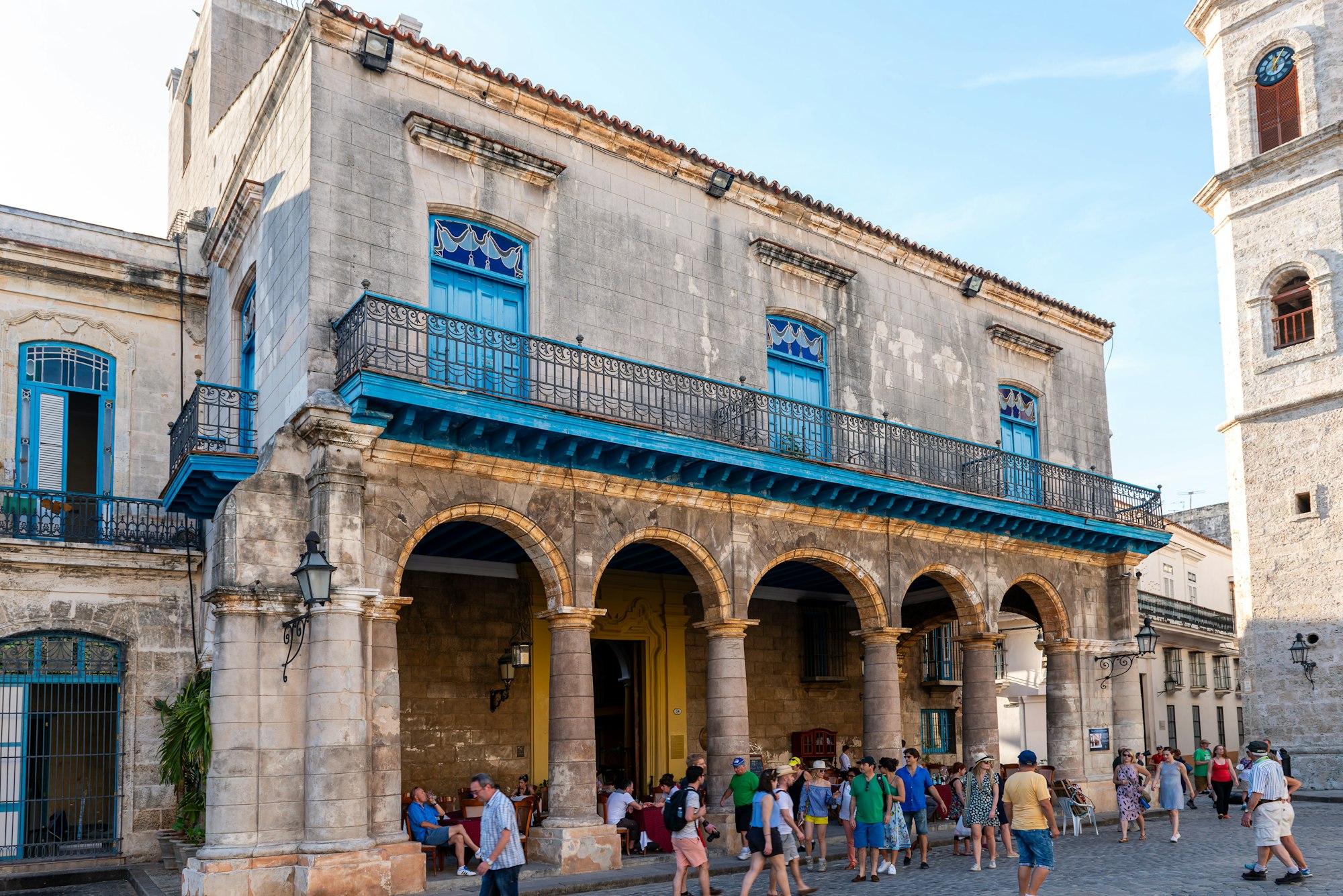 Arcaded colonial palace and cobbled square at Plaza de la Catedral in Old Havana with visitors in the foreground
