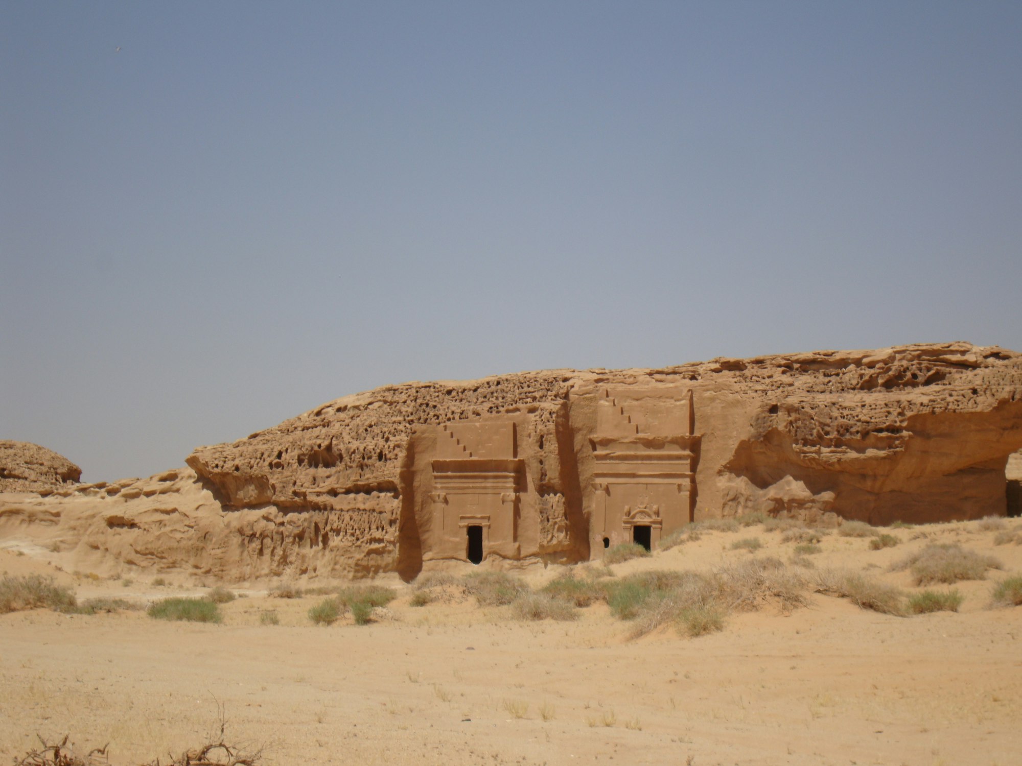 Two carved Nabataean tomb facades in a low sandstone outcrop at Hegra under flat midday light, Saudi Arabia