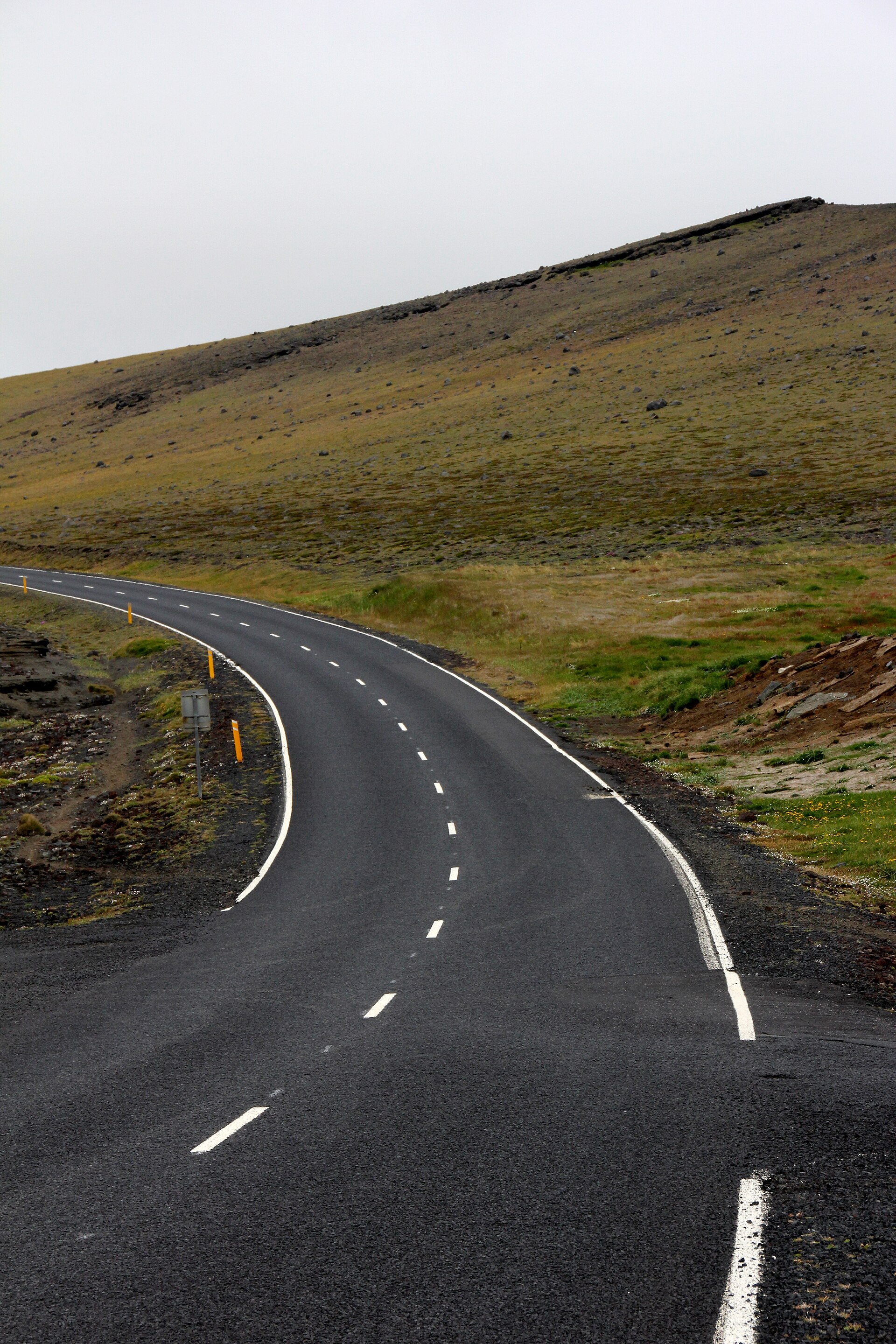 A narrow road curving over green headland ground towards Stórhöfði at the southern end of Heimaey