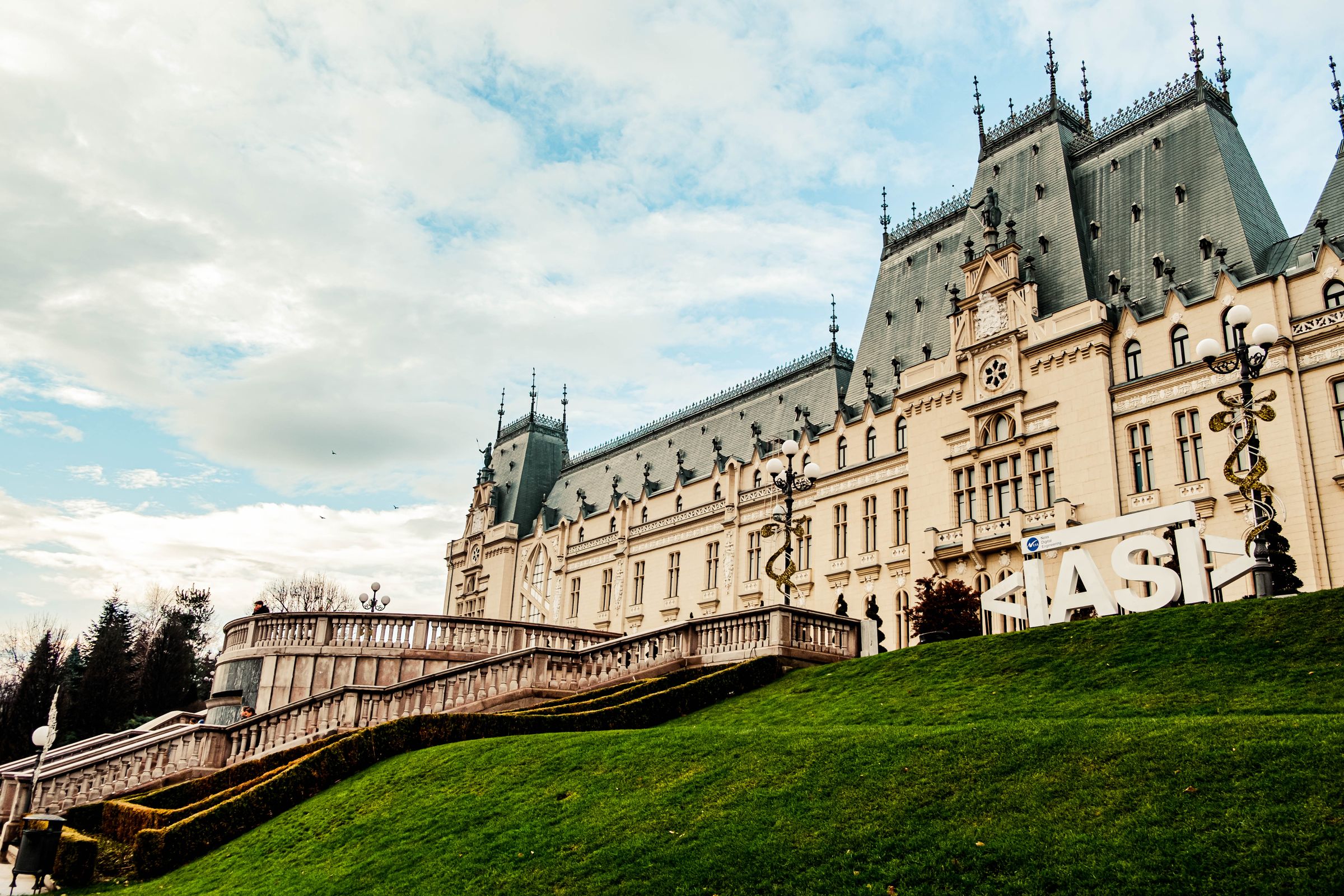The Palace of Culture in Iași, its grey spires and stone front above a steep green lawn, with the IASI letters on the slope