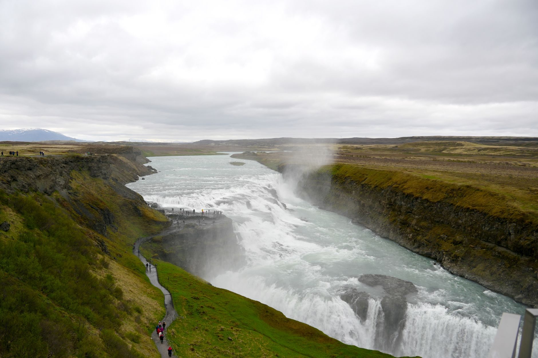 Gullfoss dropping in two steps into a narrow canyon, with a footpath along the green rim on the left