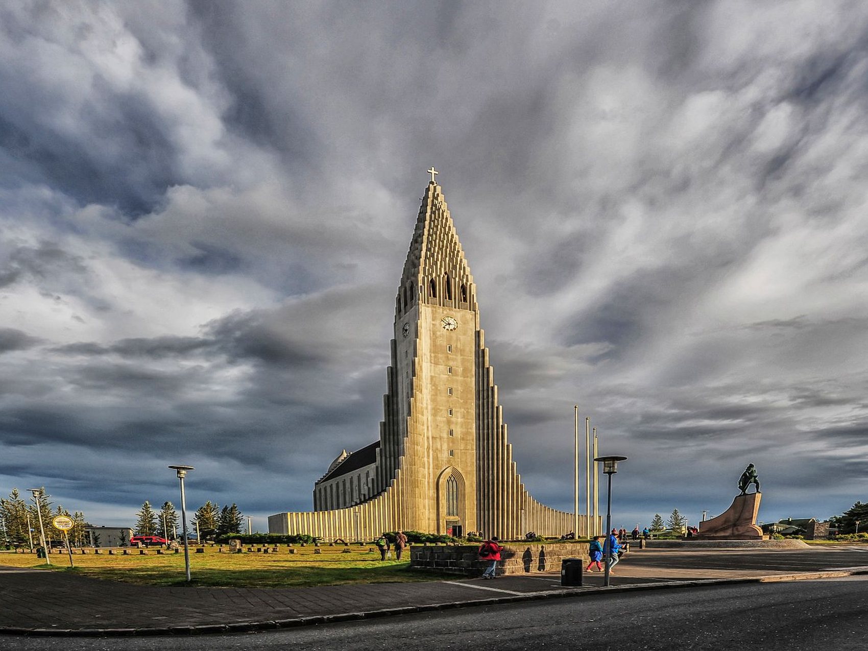 A tall pale concrete church tower with stepped flanking columns, standing alone against a dark streaked sky