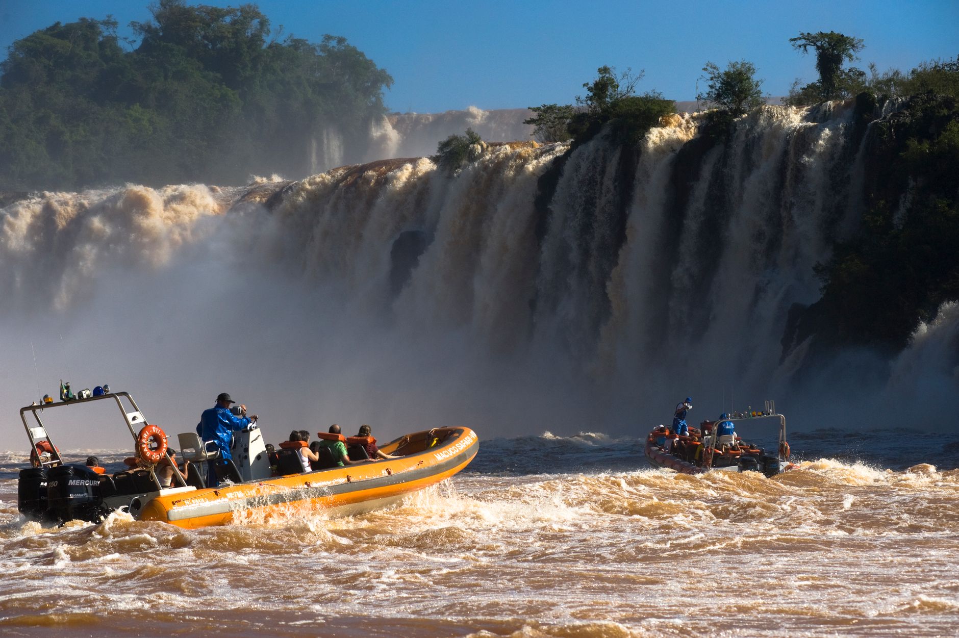 An inflatable boat full of people in the churning water at the base of Iguacu Falls, spray everywhere
