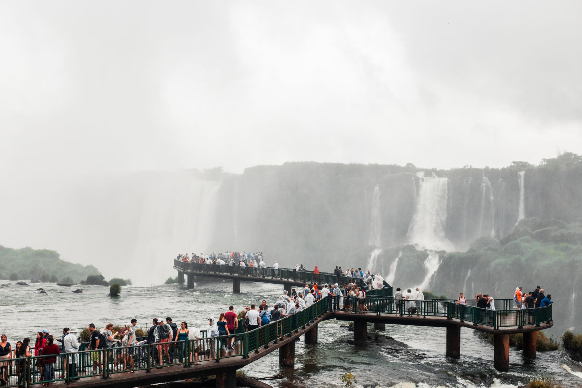 Visitors on a steel catwalk extending into the mist at the base of Iguacu Falls, spray rising around them