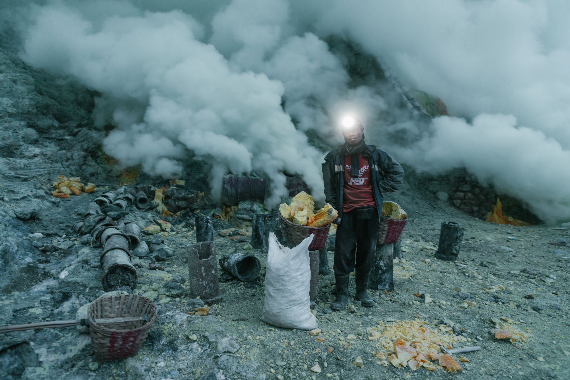 A sulphur miner with baskets on the dark trail at Kawah Ijen, lit by a headlamp