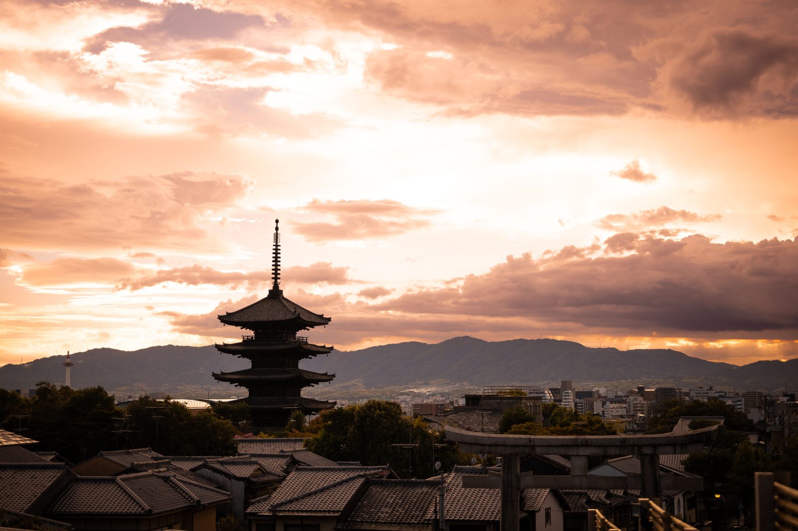 The five storey Yasaka Pagoda rising above tiled roofs in Kyoto at sunset, the sky orange behind it