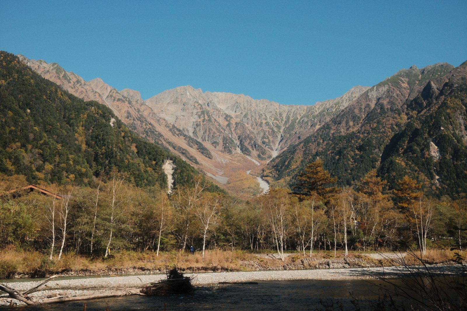 The Hotaka range seen from Kamikochi in Nagano in autumn, bare rock peaks above a forested valley turning gold