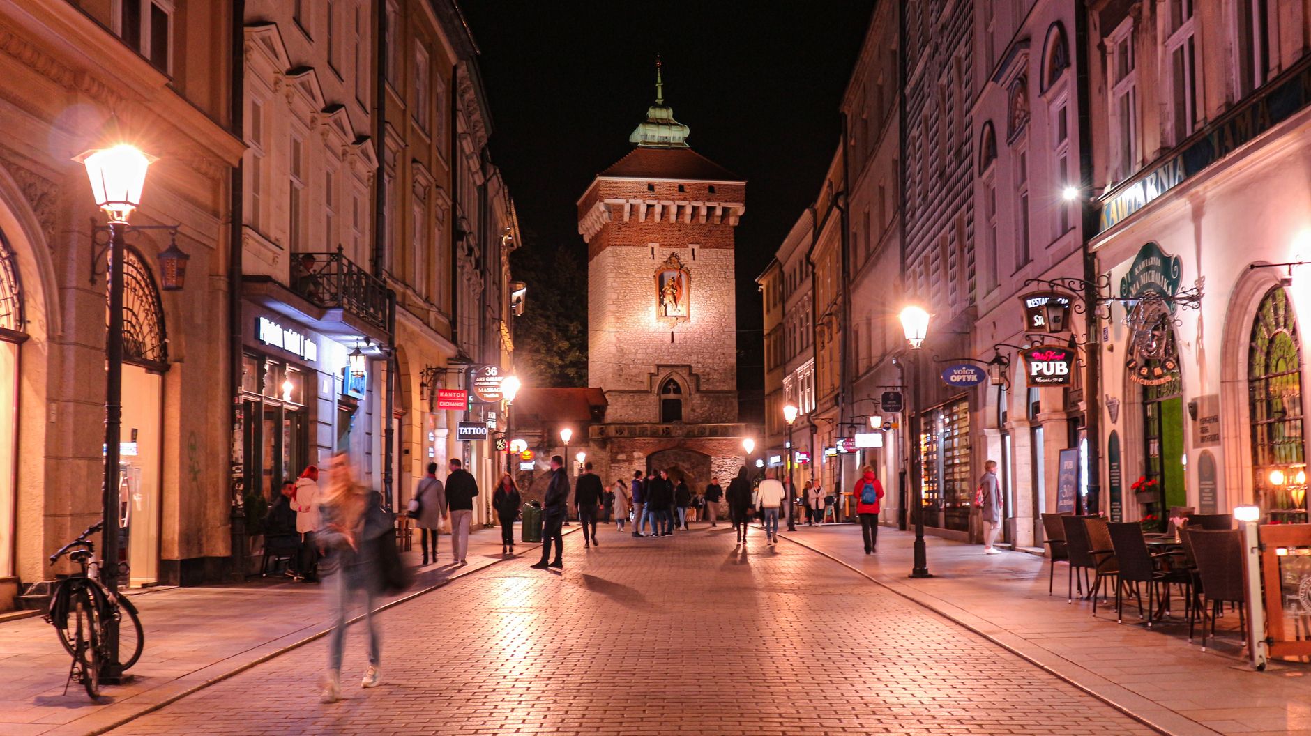 Floriańska Street in Krakow at night, lit shopfronts with Polish signage and St Florian's Gate at the end