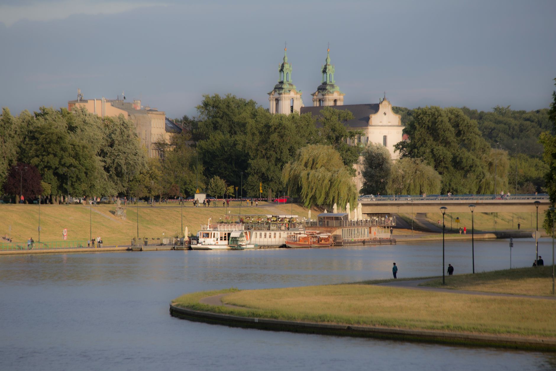 The Vistula river in Krakow with wooded banks, a moored boat and a green-domed church on the skyline