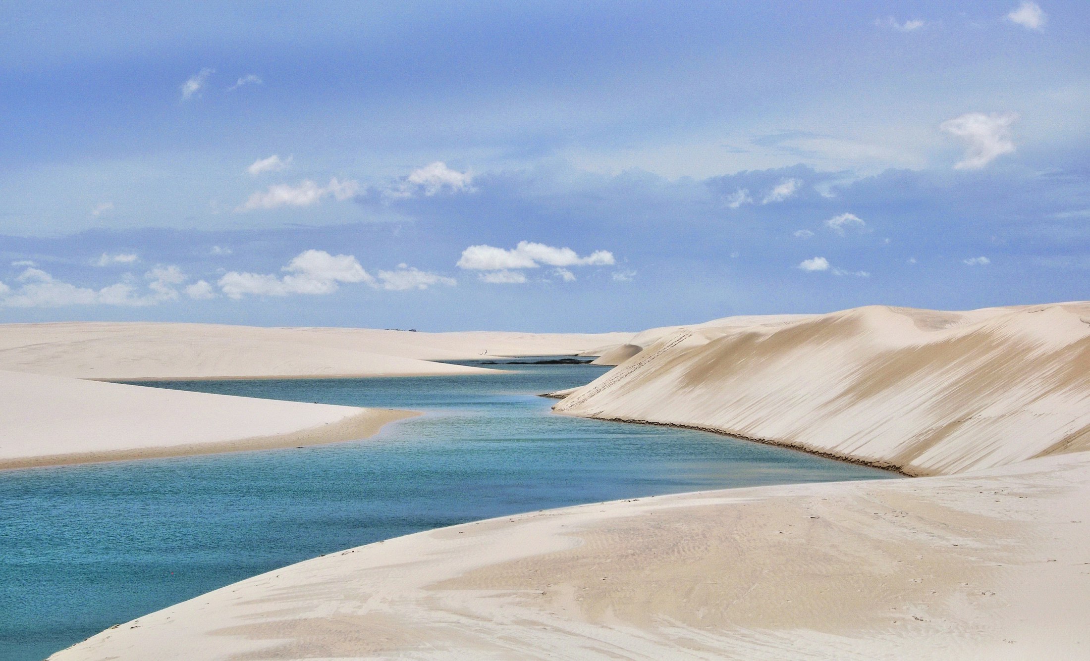 A clear blue-green lagoon held in a hollow between white sand dunes
