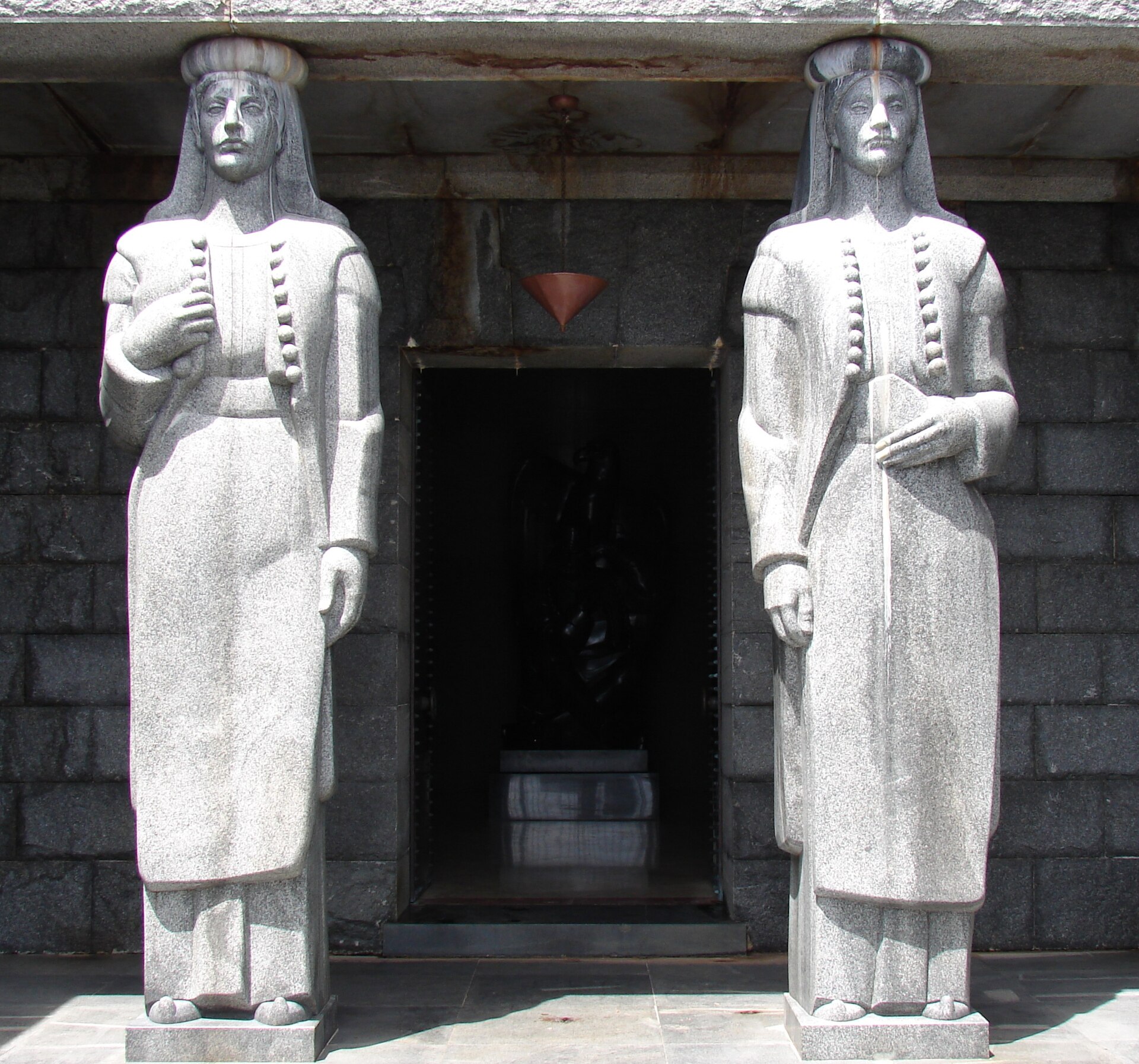 Two tall granite female figures in Montenegrin dress standing either side of the doorway of the mausoleum, carrying the lintel