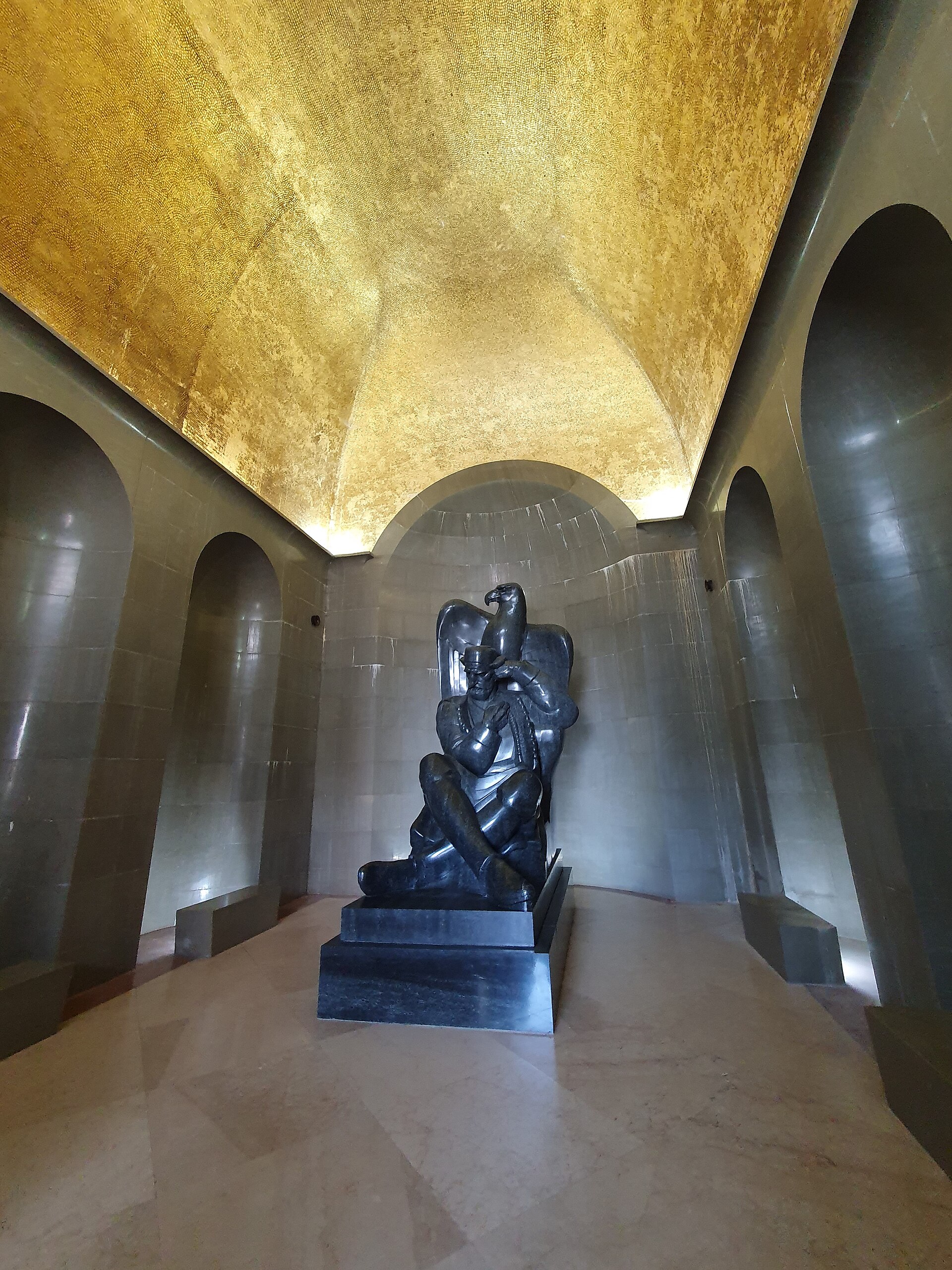 The seated granite figure of Njegoš beneath a gold mosaic vault, an open book on his lap and an eagle above him