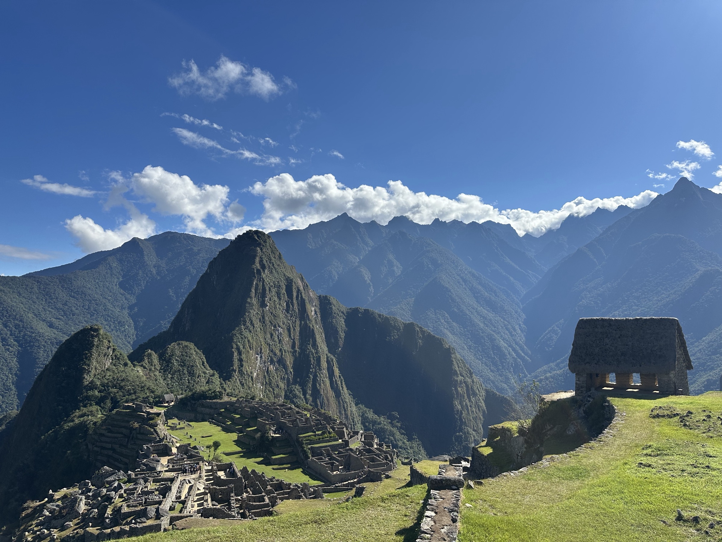 The stone ruins of Machu Picchu with the caretaker's hut and the Andes ridge behind under cloud