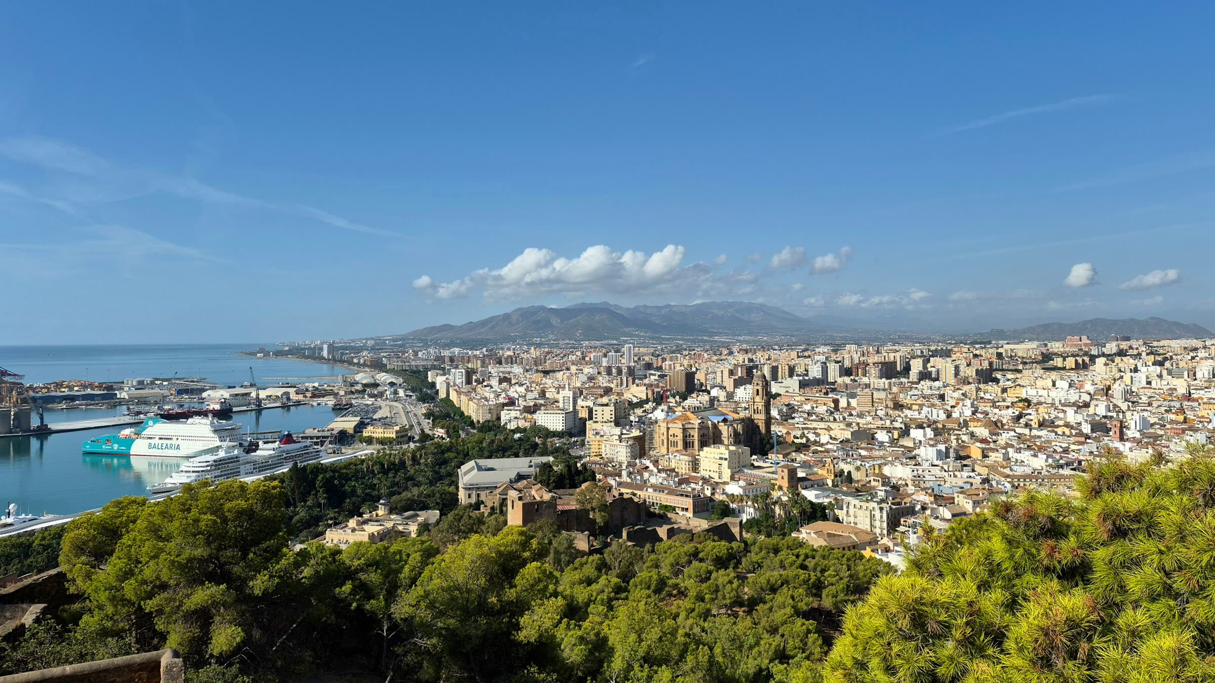 Málaga from the Gibralfaro hill, the port and a ferry on the left, the cathedral with its single tower in the middle of the old town and the mountains behind