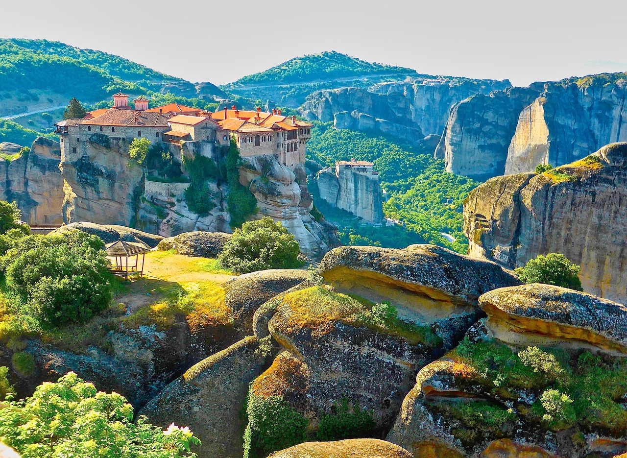 A red roofed monastery compound on a broad rock summit at Meteora with the wider pillar field and a second monastery behind