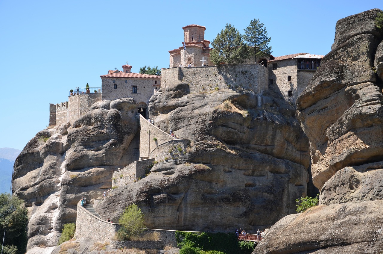 Visitors climbing a walled stone stairway cut up the rock to a monastery gate at Meteora