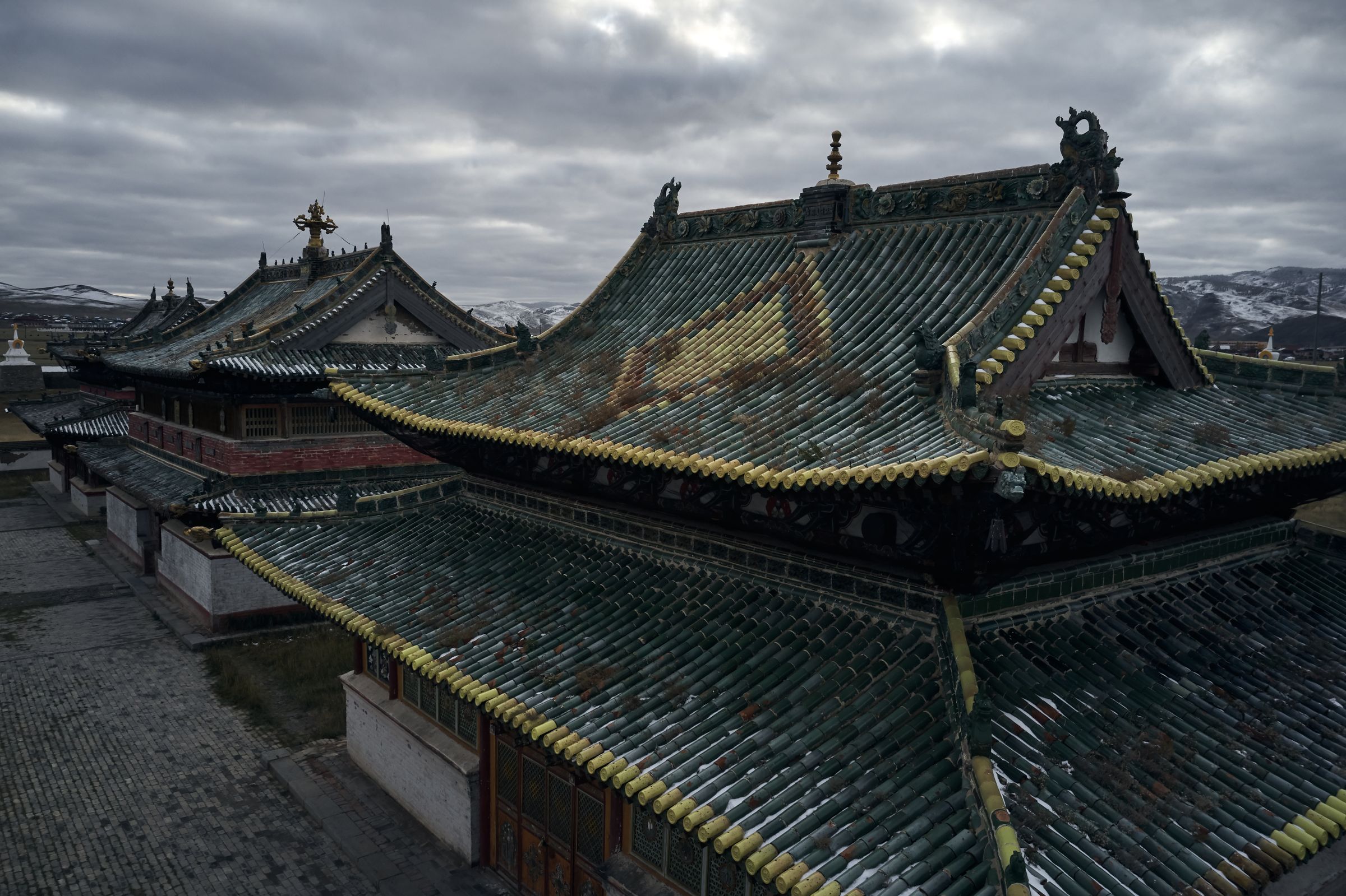 The green-tiled temple roofs of Erdene Zuu monastery and its white stupa wall beneath snow hills
