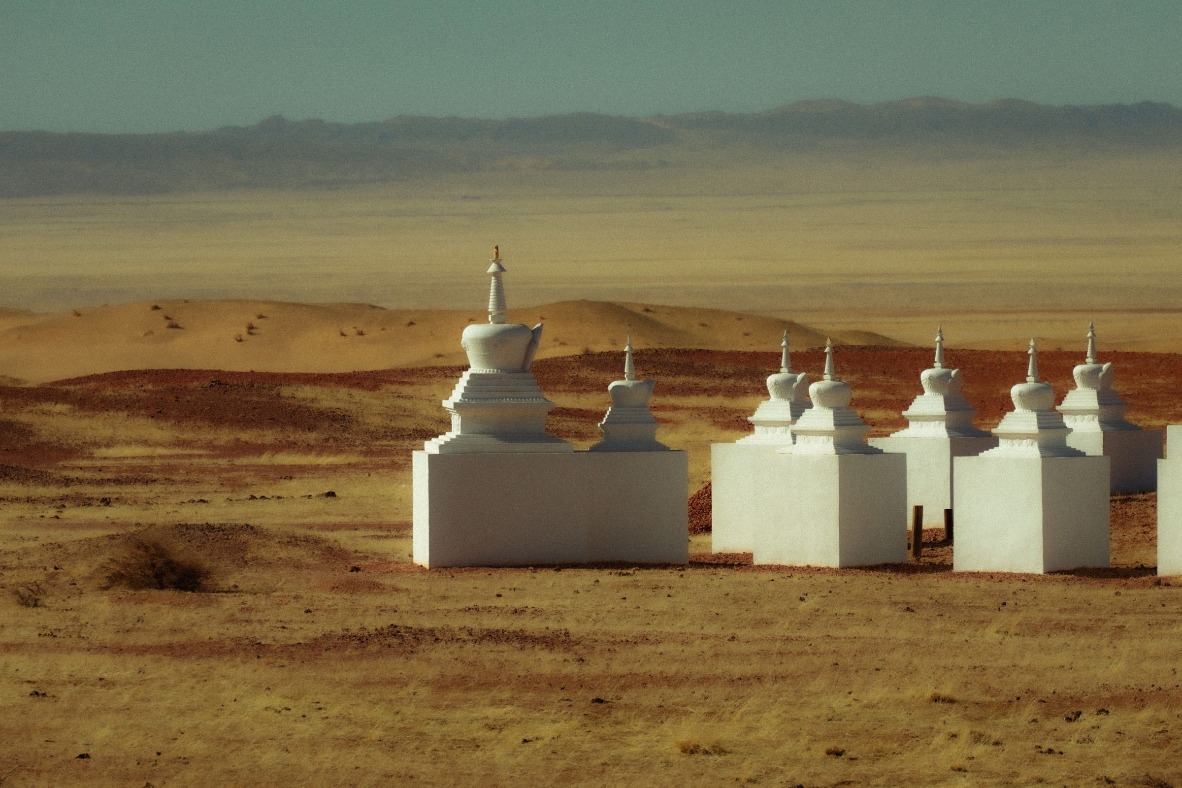 White stupas standing on open ground under a hazy sky on the Mongolian steppe