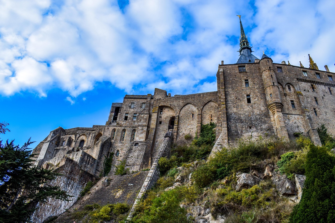 The abbey church and spire of Mont-Saint-Michel seen from below against a blue sky