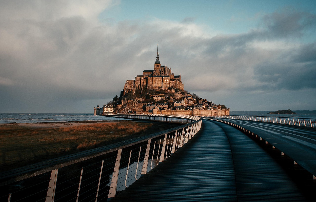 The stilted footbridge curving across the sand toward Mont-Saint-Michel under a grey sky
